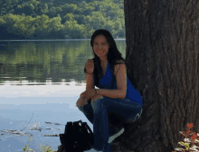 a woman leans against a tree near a body of water