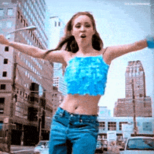 a woman in a blue crop top and blue jeans is dancing in a city