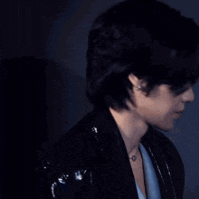 a close up of a young man wearing a necklace and a jacket .