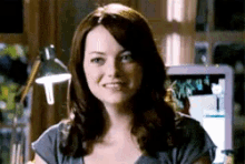a woman in a grey shirt is smiling in front of a computer
