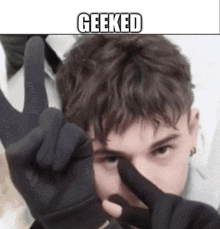 a young man wearing a pair of black gloves is making a peace sign with his fingers .