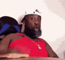 a man with a beard is wearing a red tank top and a white hat .