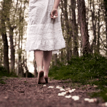 a woman in a white dress is walking barefoot down a path in the woods