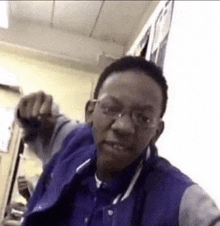 a young man wearing glasses and a blue jacket is making a funny face in a classroom .
