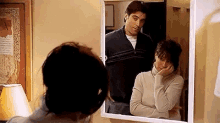 a woman is looking at her reflection in a mirror while a man stands behind her .