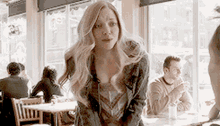 a woman is standing in a restaurant with a man sitting at a table .