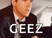 a man in a suit and tie is sitting in the back seat of a car with the word geez on the screen .