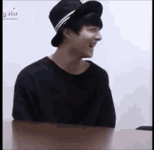 a young man wearing a hat is sitting at a table and smiling .