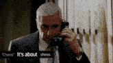 a man in a suit is talking on a phone with the words " chess " it 's about chess below him