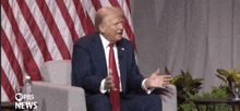 a man in a suit and tie sitting in front of an american flag