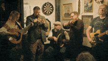 a group of musicians are playing in a room with a dart board on the wall behind them