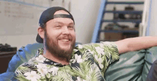 a man with a beard is sitting on a bean bag chair wearing a hat and a hawaiian shirt .