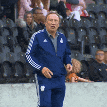 a man wearing a blue adidas jacket stands in a stadium