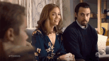a man and a woman are sitting on a couch talking to each other . the woman is smiling .