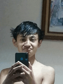 a shirtless young boy is taking a selfie with his phone .