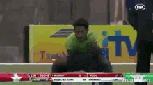 a man in a green shirt is squatting down on a field in front of a fox tv advertisement .