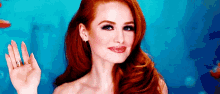 a woman with red hair is standing in front of a blue background and waving .
