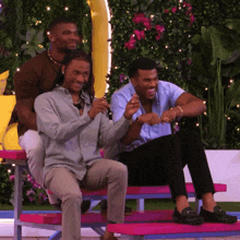 three men are sitting on a pink bench and one of them is holding an inflatable banana