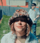 a woman wearing a leopard print hat and a fur coat is standing next to a man wearing sunglasses .