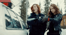 two women are standing next to a car with the word hw on the bottom