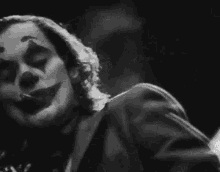a black and white photo of a clown smoking a cigarette in a dark room .