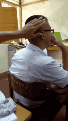 a man in a white shirt sits at a desk with a number 153 on the back of his chair