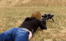 a woman in jeans is laying on the ground holding a rifle .