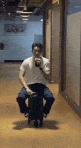 a man is sitting on a suitcase in a hallway and drinking from a cup