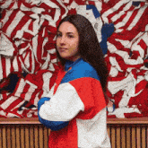 a woman in a red white and blue jacket is standing in front of a pile of red white and blue striped shirts .