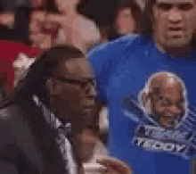a man wearing a blue shirt with a picture of a man on it is covering his face with his hands .