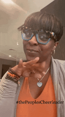a woman wearing glasses and a necklace has the hashtag #thepeoplescheerleader