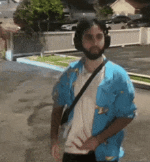 a man with a beard wearing headphones and a blue shirt is walking down the street .