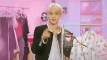 a man in a black jacket is standing in front of a pink wall holding a bag .