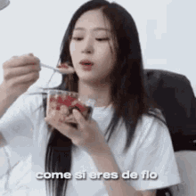 a woman is eating a dessert with a spoon and a cup of strawberries .