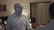 a man wearing glasses and a white shirt talks to another man