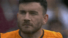 a close up of a man 's face with a beard wearing an orange shirt