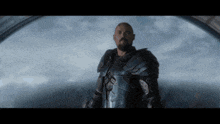 a man with a beard is wearing armor and looking out of a window