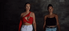 two women are standing next to each other in front of a dark wall .