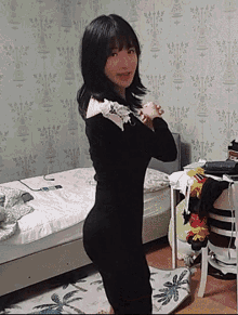 a woman in a black dress is standing in a bedroom next to a bed and a table .