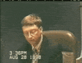 a man in a suit and tie sits in a chair at 3:37 pm august 28 1998