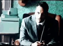 a man in a suit sits in a chair with his hands folded
