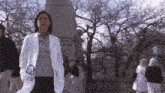a woman in a white coat with a stethoscope around her neck is walking in a park .