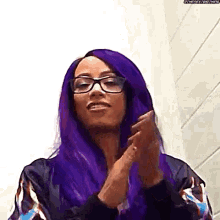 a woman with purple hair and glasses is clapping her hands in a bathroom .