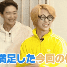 a man wearing glasses and a yellow adidas jacket is smiling next to another man