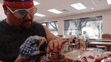 a man wearing sunglasses and a bandana is eating a chicken sandwich