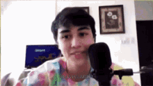 a young man is talking into a microphone while wearing a colorful tie dye shirt .