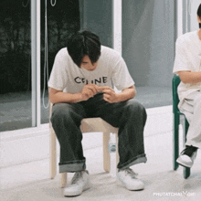 a man wearing a white celine shirt sits on a chair