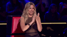 a woman in a black dress is sitting in a chair and clapping