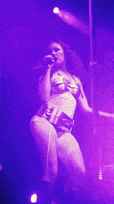 a woman singing into a microphone while wearing a purple outfit