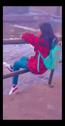 a girl with a blue backpack is sitting on a railing overlooking the ocean